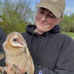 Loren holding an owl out side, wearing a black sweatshirt and dark canvas had