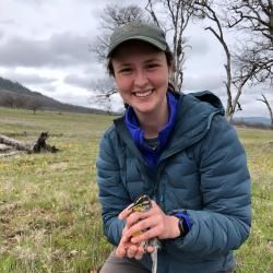 Sam kneeling in the grass with a bird in her hands