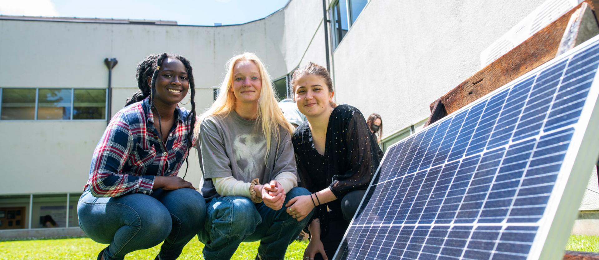three female students squatting next to a solar array