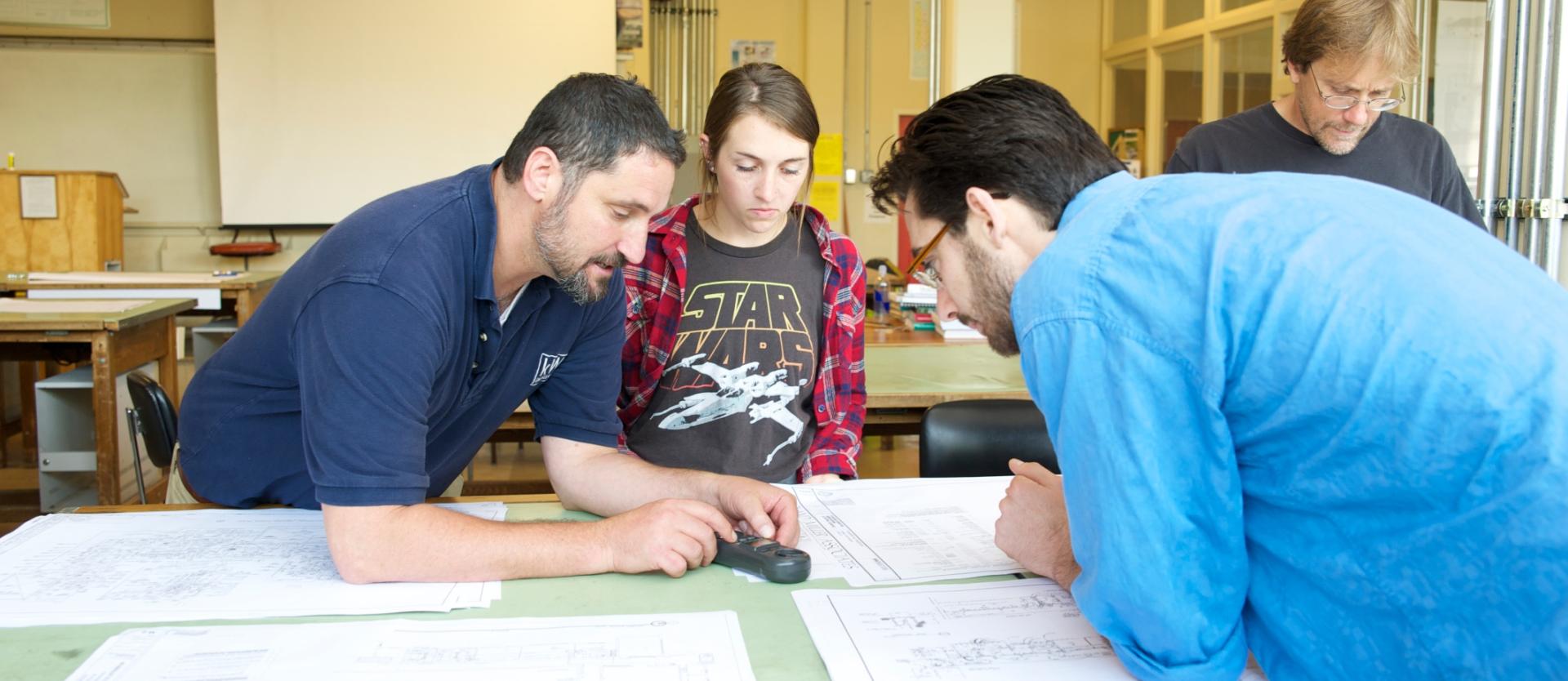 two students and a professor looking at papers and piece of equipment on a table