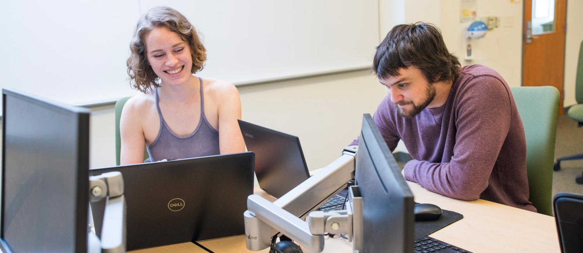 two students sitting next to a computer smiling