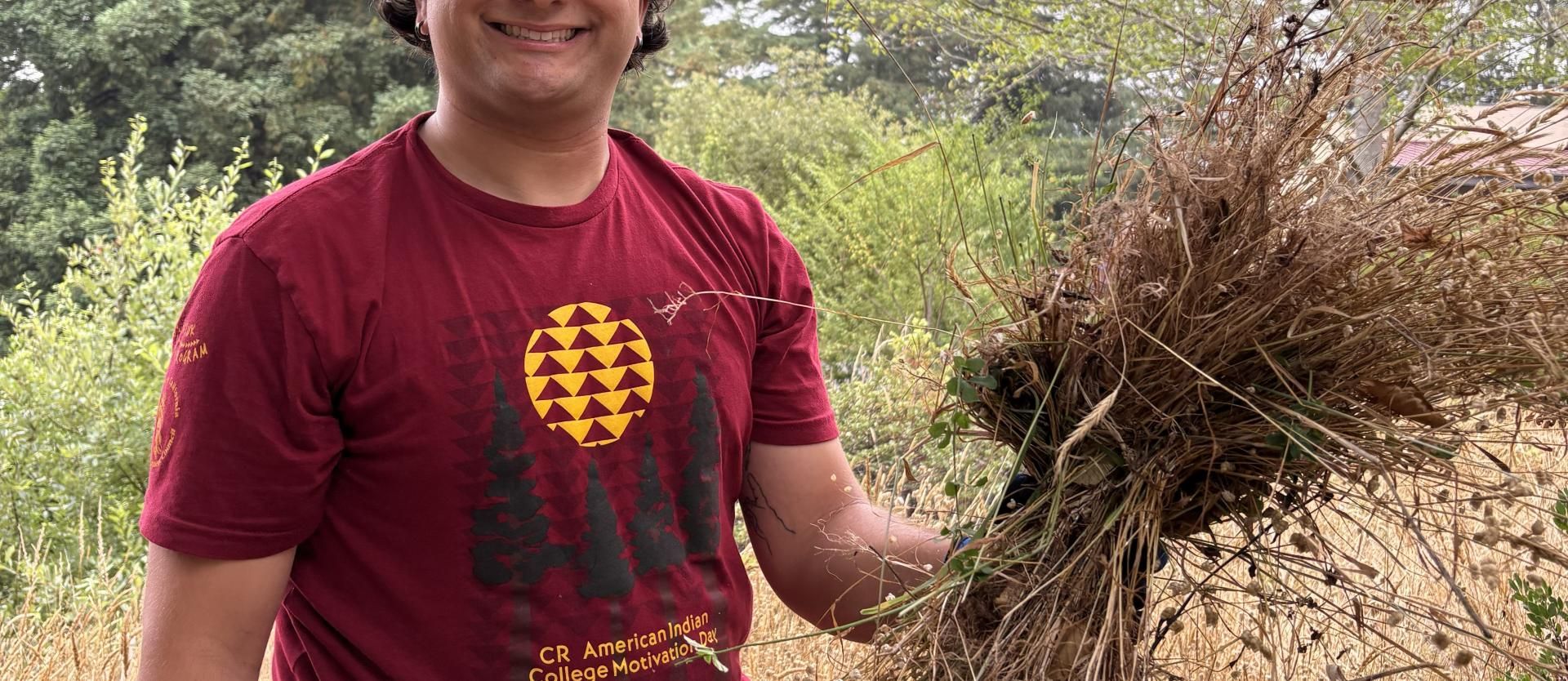FSL Student Research Assistant Joe holding up weeds pulled in the Indigenous Garden Area