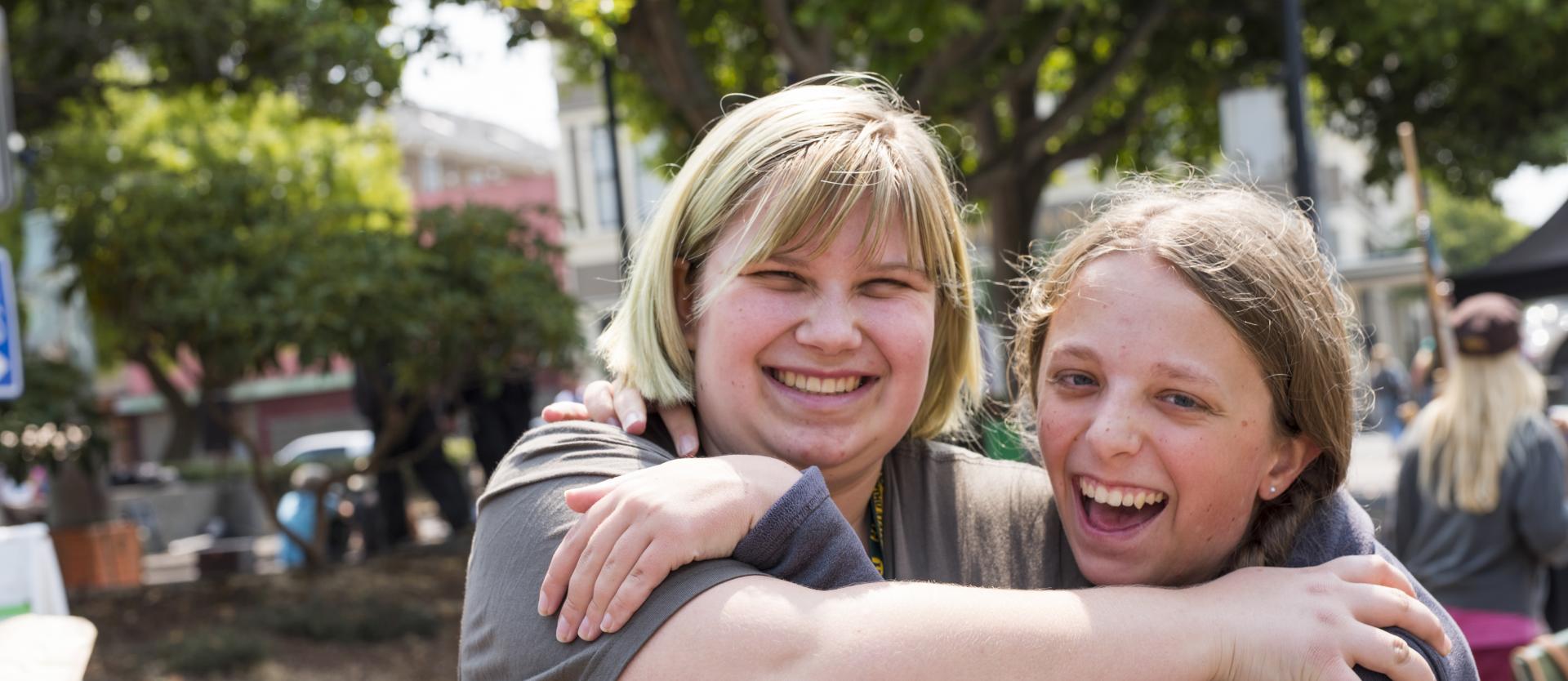 Two students hugging and laughing on a sunny day