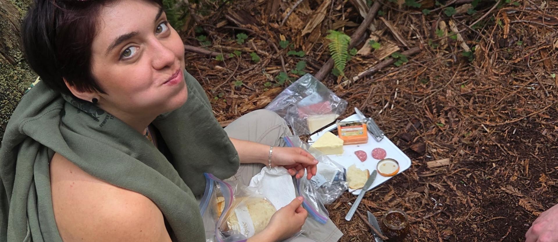 Backpacker awkwardly smiling at the camera as she enjoys her snack.