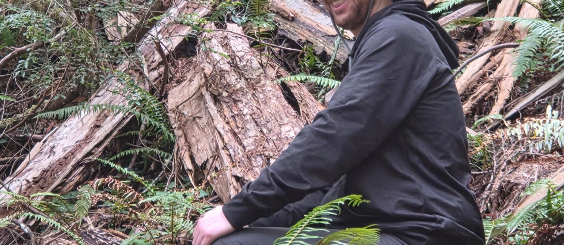 Backpacker happily sitting on a downed log.