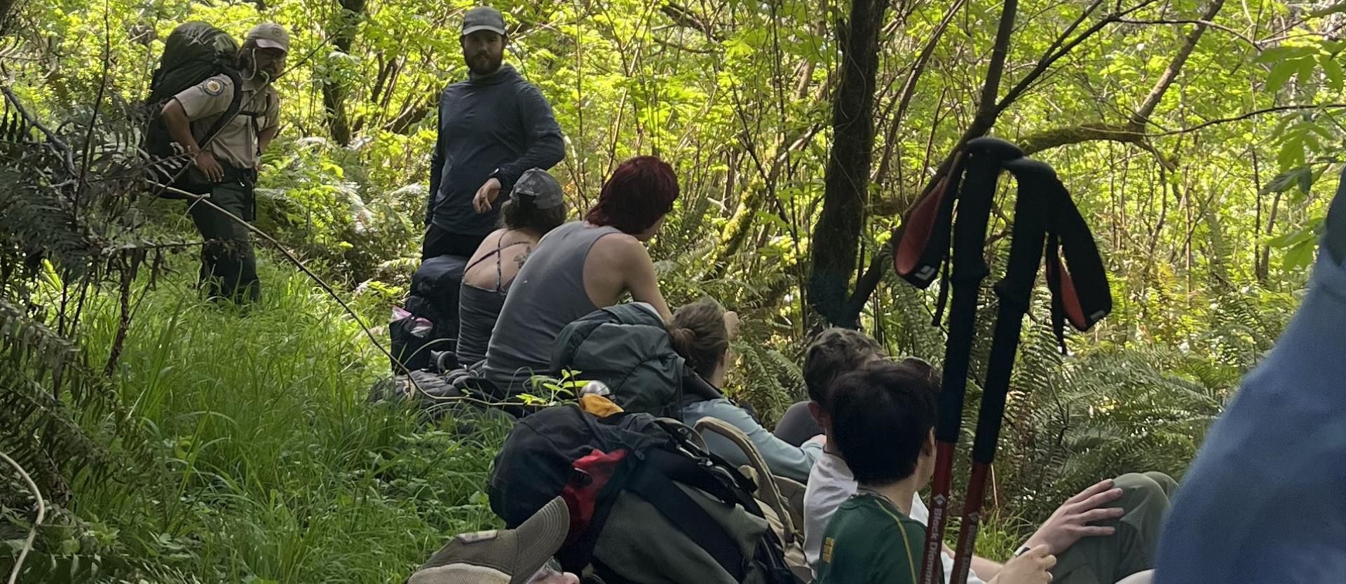 Group of backpackers sitting on the forest trail relaxing for a quick break.