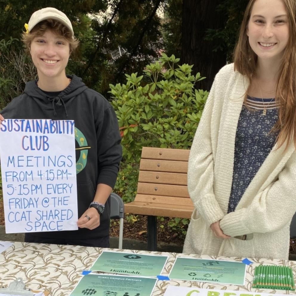 two students at a table, one holding a poster