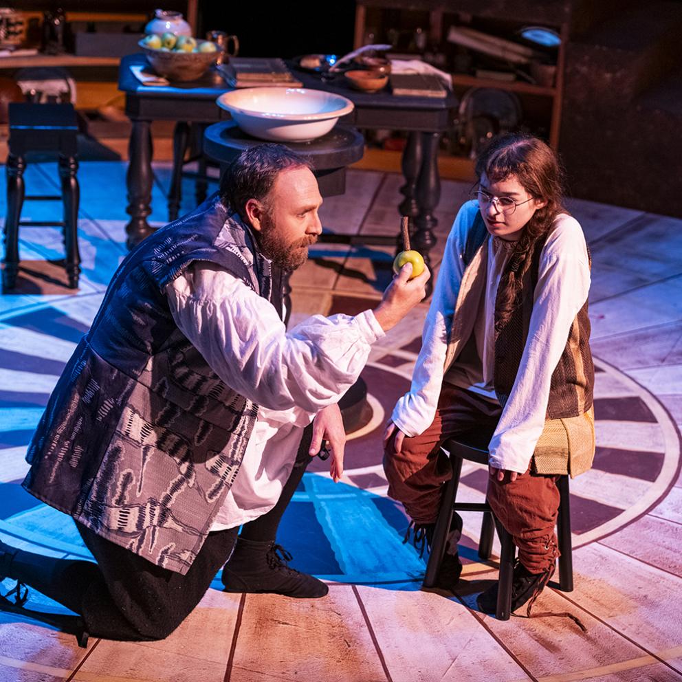 a man acting on stage showing an apple to a girl