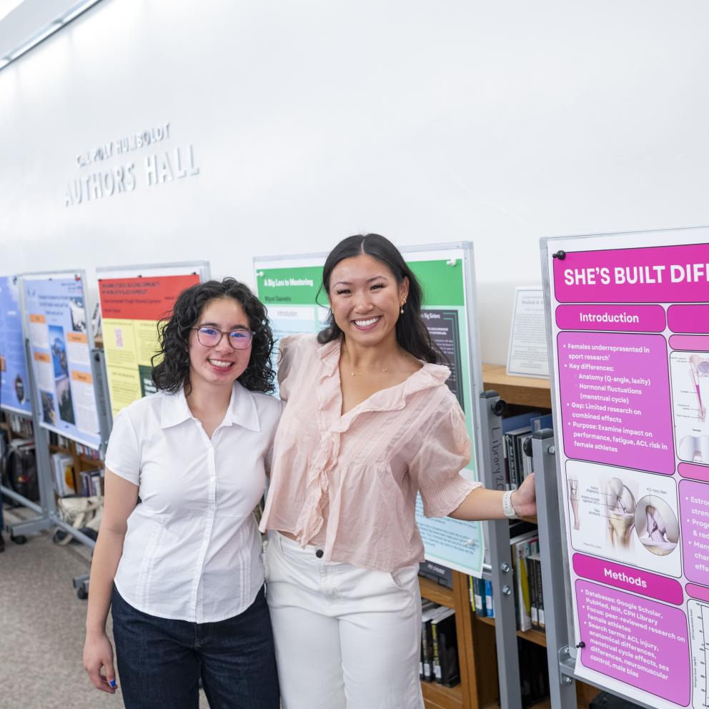 Two female students one wearing glasses, presenting poster at ideafest
