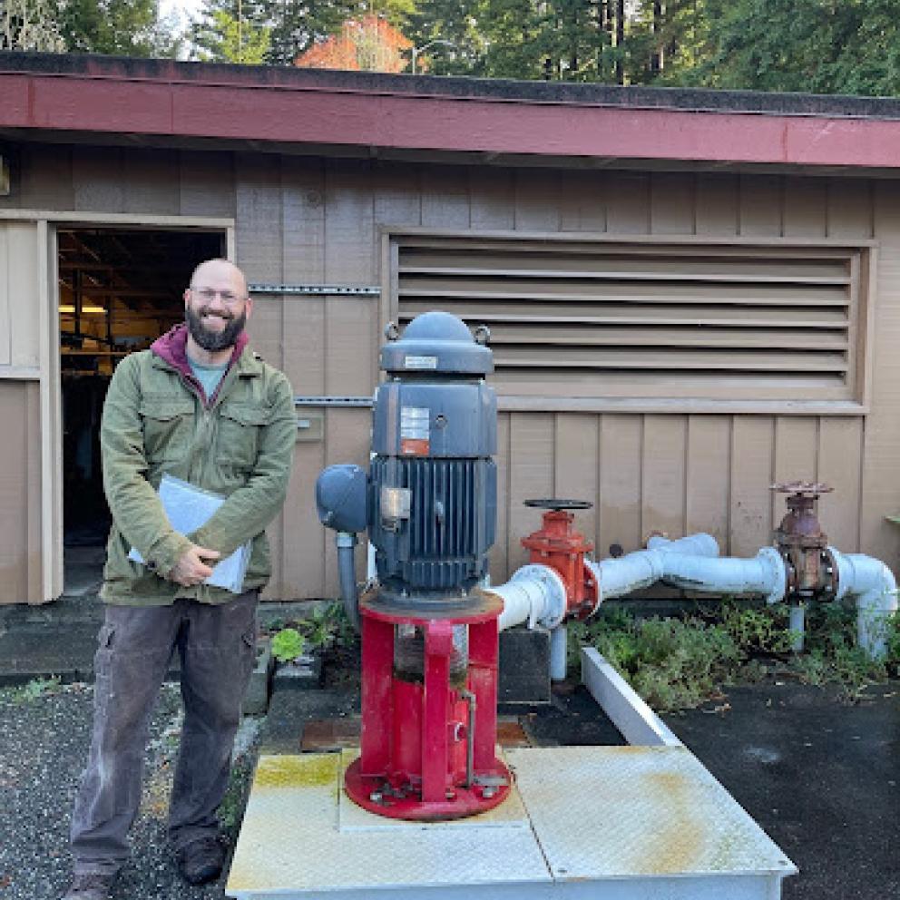 Image shows Fisheries Technician Patrick Nero smiling on the left side of a replaced pump. 