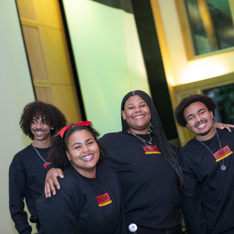 Image shows a group of four team members from Umoja smiling and standing shoulder to shoulder in black crewneck sweatshirts. 