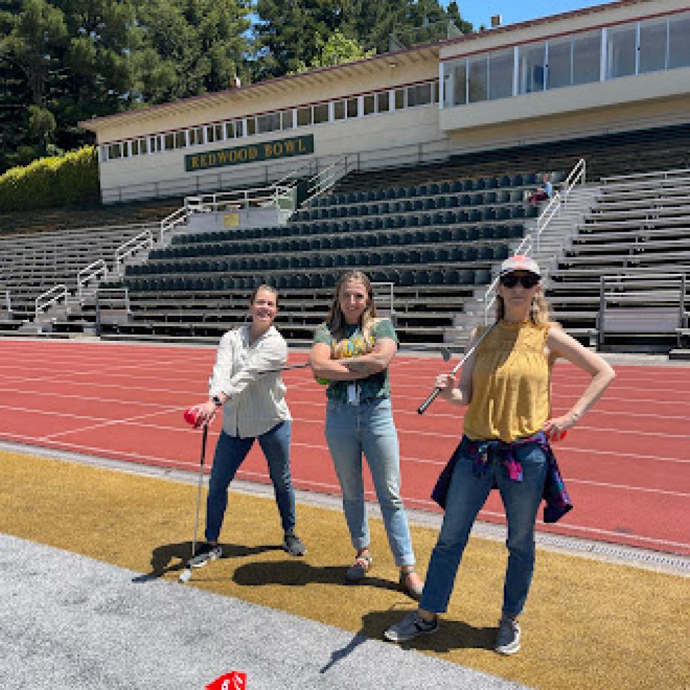 Three women holding minigolf clubs in redwood bowl