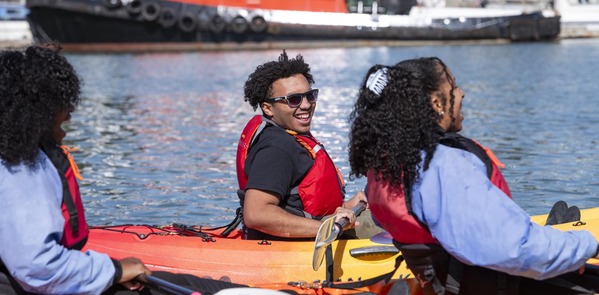 Two students laugh while kayaking next to each other.