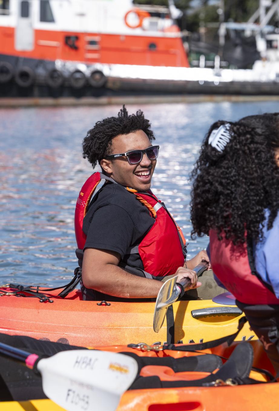 Two students laugh while kayaking next to each other.