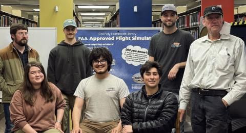 A group of people standing by the flight simulator, including students and the faculty advisor of the aviation club.