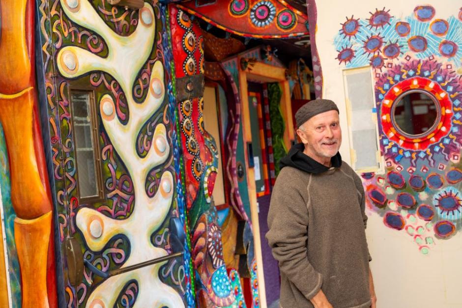 A photo of artist David White posing in front of the art hallway he created. 