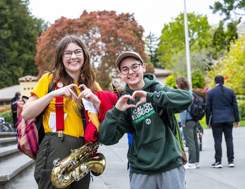 A photo of two students holding up their hands as hearts on campus. A photo of two students holding up their hands as hearts on campus.