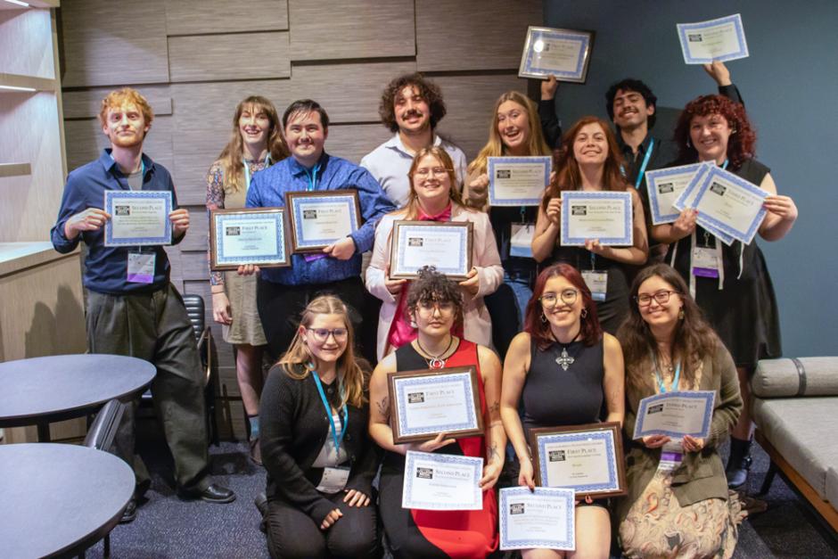 more than a dozen journalism students stand together holding their awards