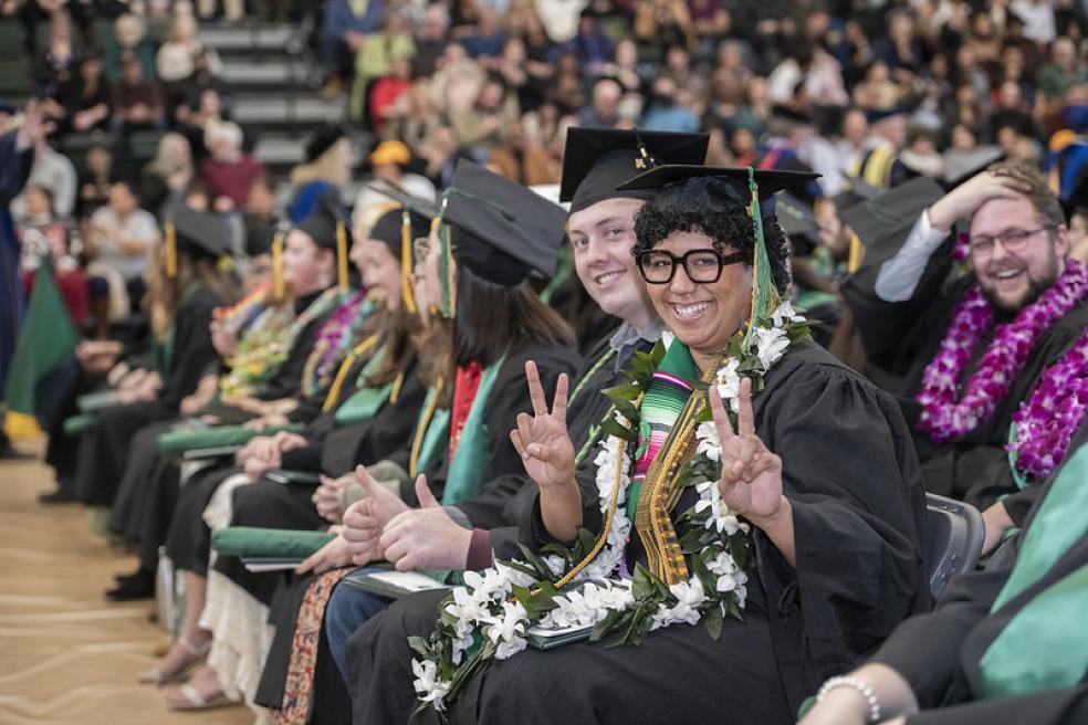 graduates in their caps and gowns flashing a peace sign at the camera