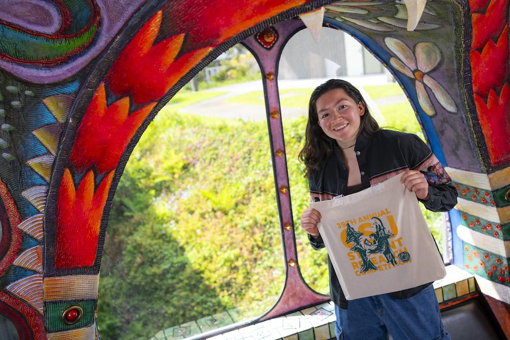 student holds up a tote bag with her logo design on it