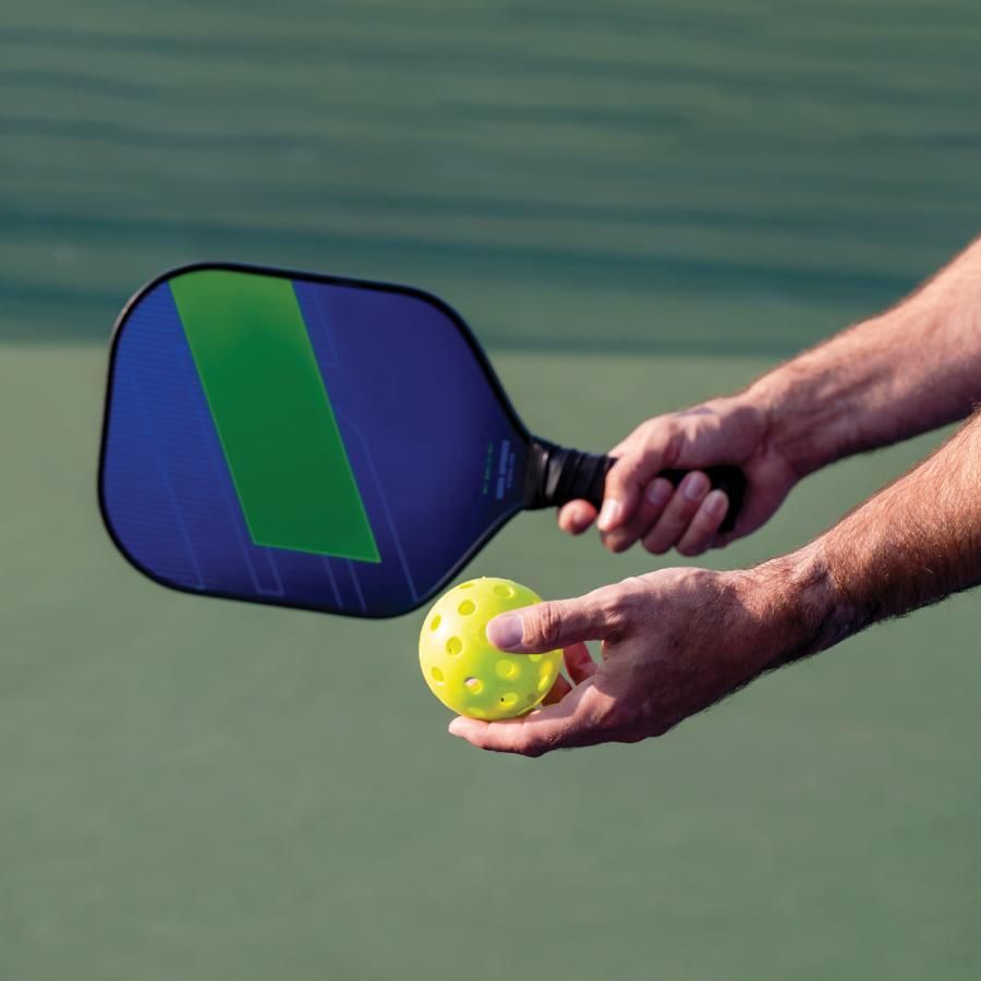 Hand holding a pickleball racket and ball
