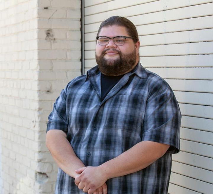 Felix, standing next to a building wearing a blue plaid shirt