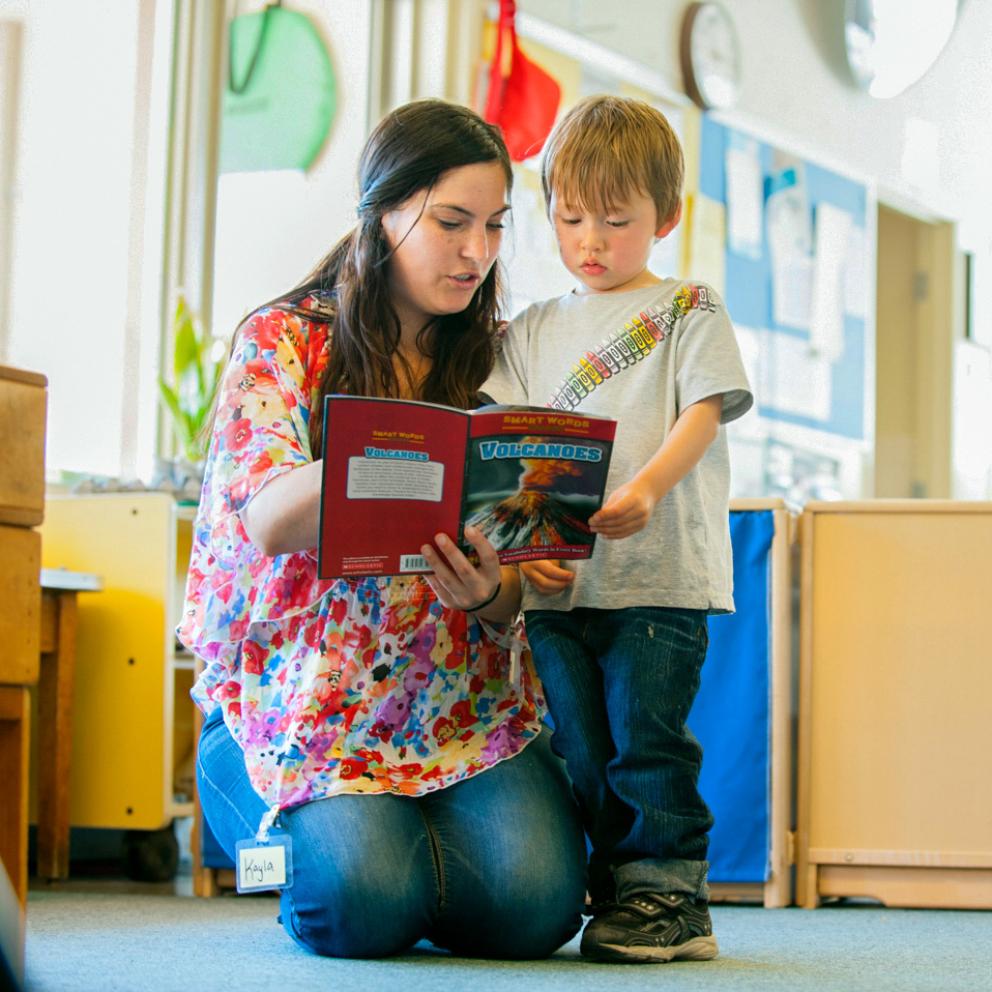 student on her knees read to a child