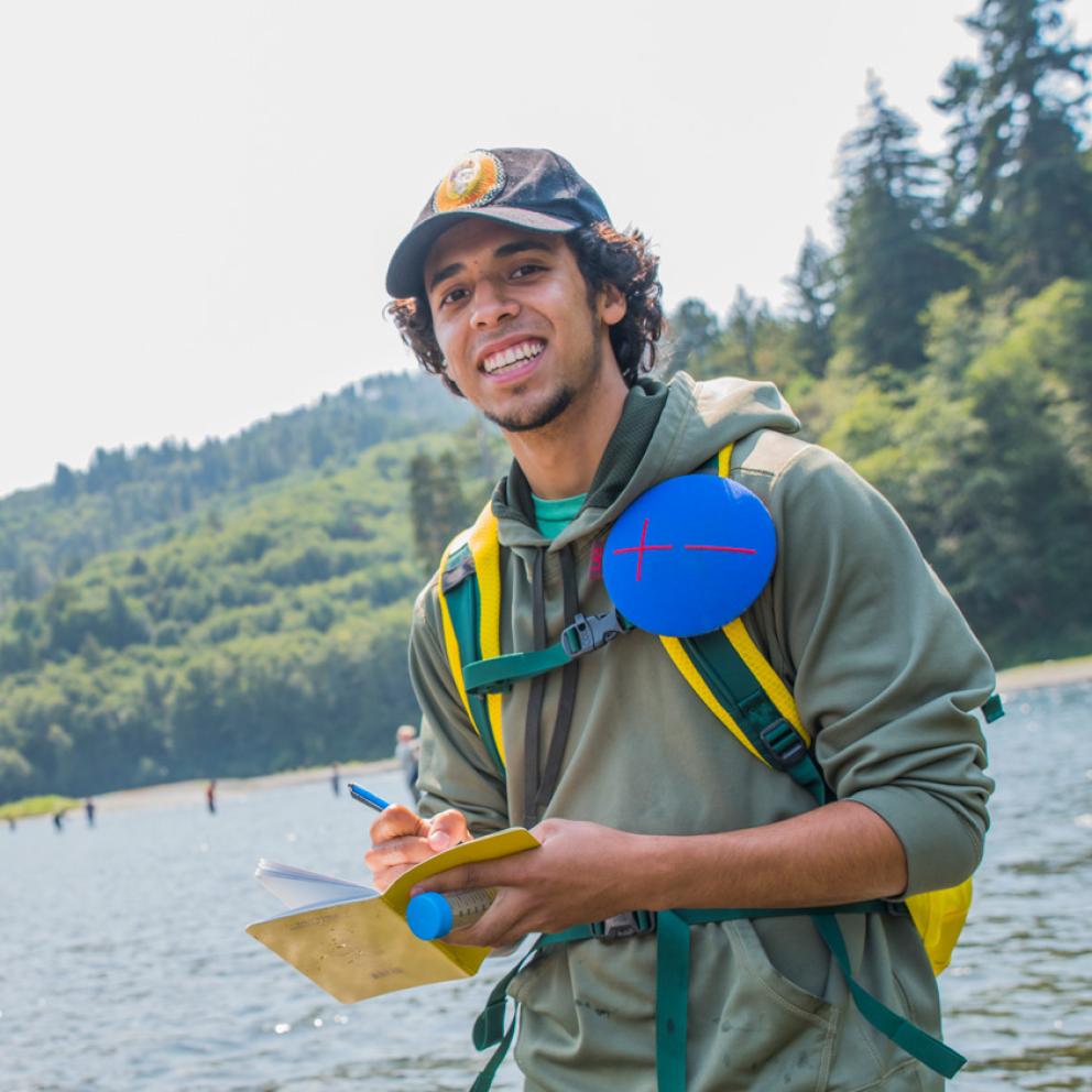 Student standing in a river with a notebook looking at the camera