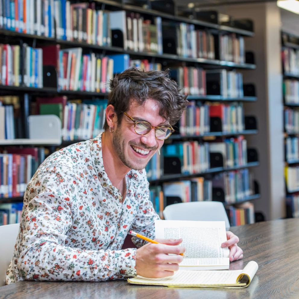 student in the library sitting in front of books smiling