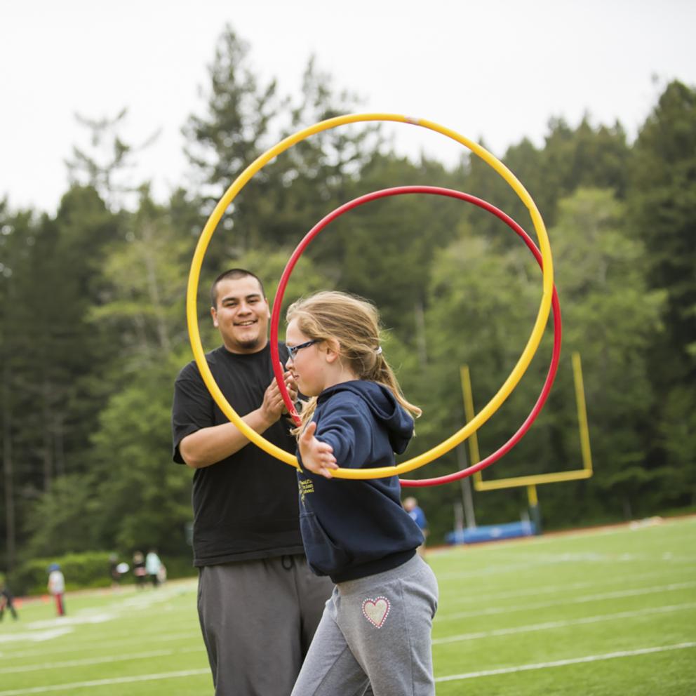Student with hula hoops assisting a younger child