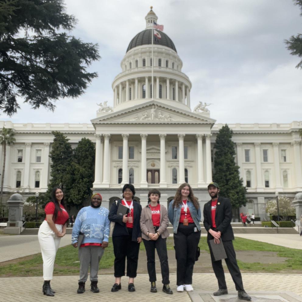 Six students wearing CSSA t-shirts stand before the California capitol building