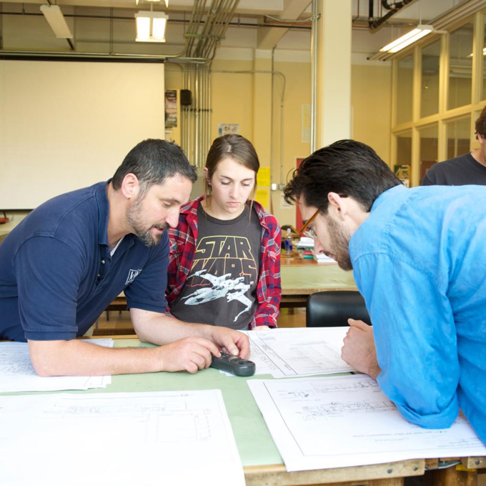 Two students and a professor hovering over a table reading some documents