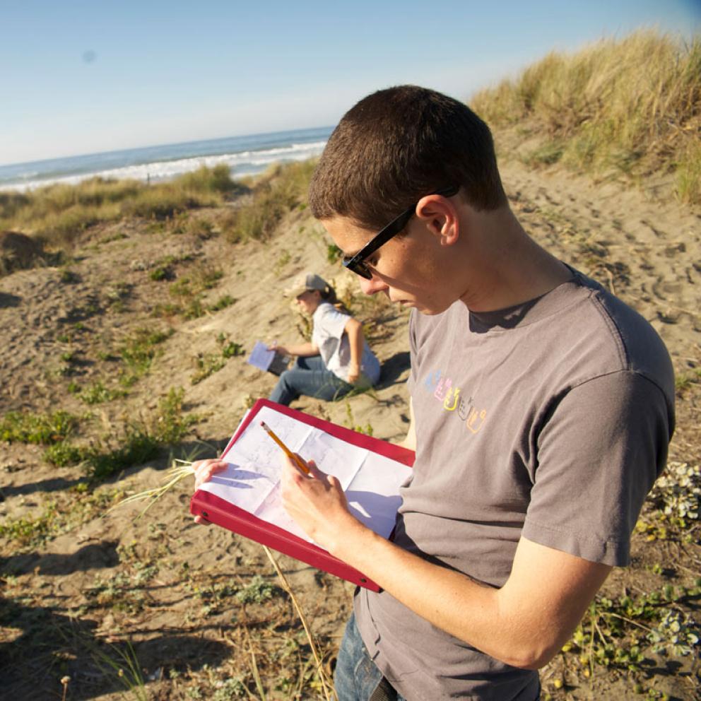 student writing in a notebook at the beach