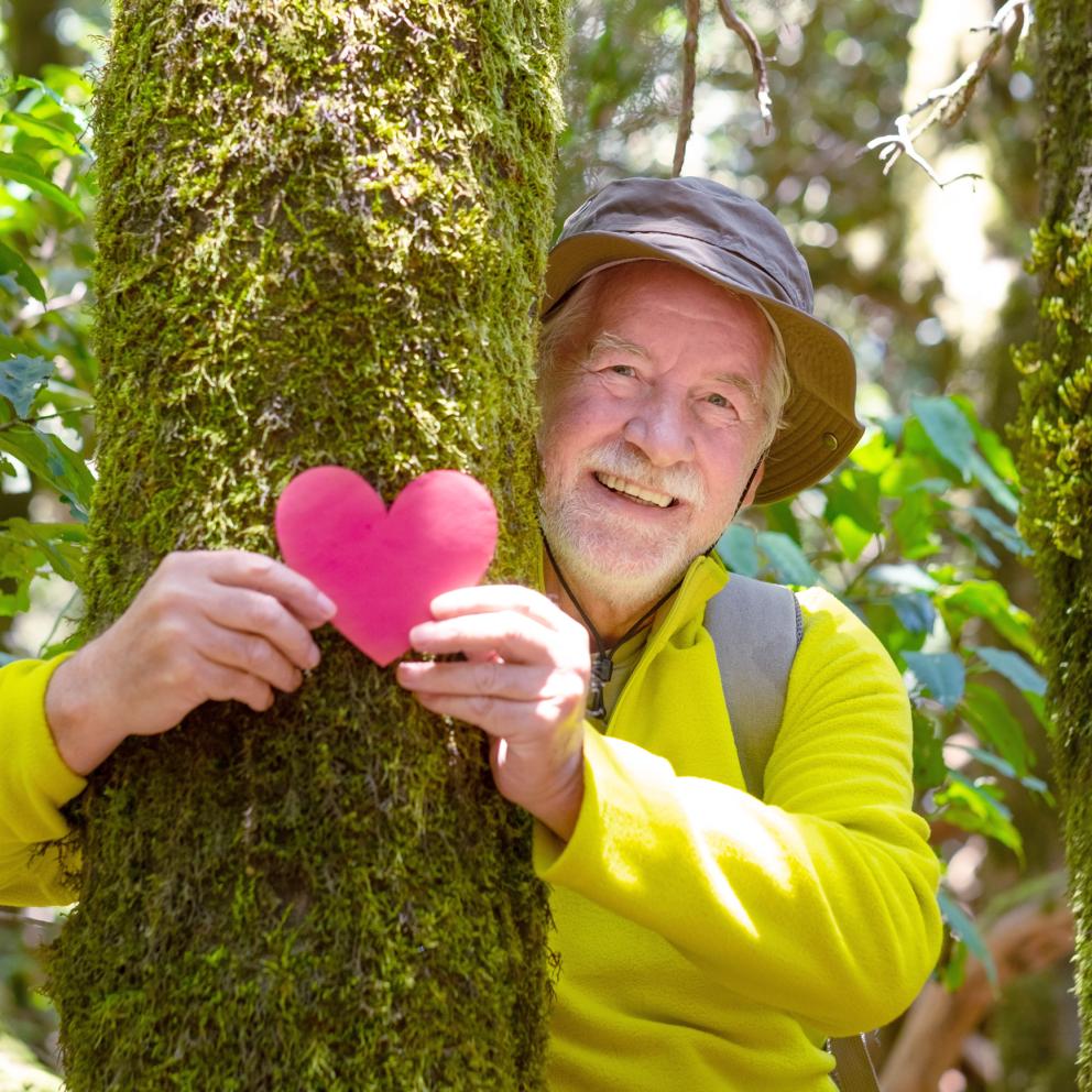 Man holding paper heart, arms around a tree