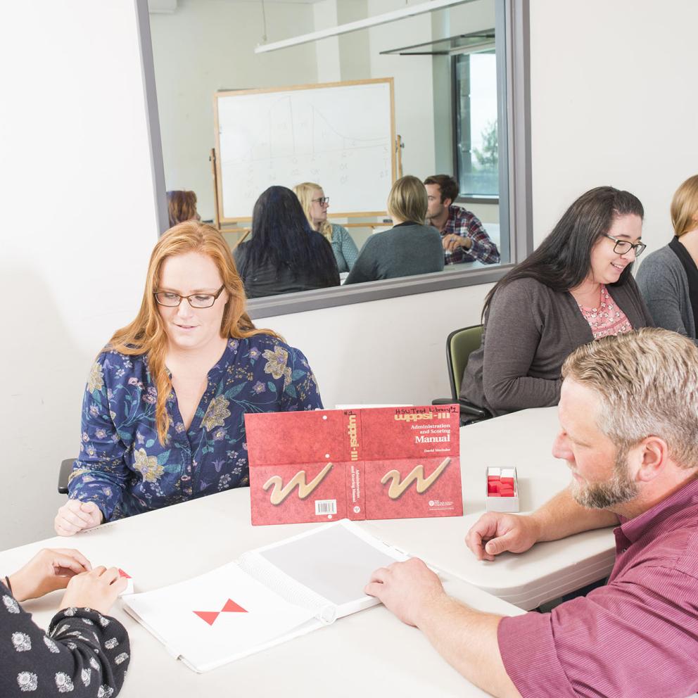 Psychology students in a room sharing books and a wall with one sided glass for observation