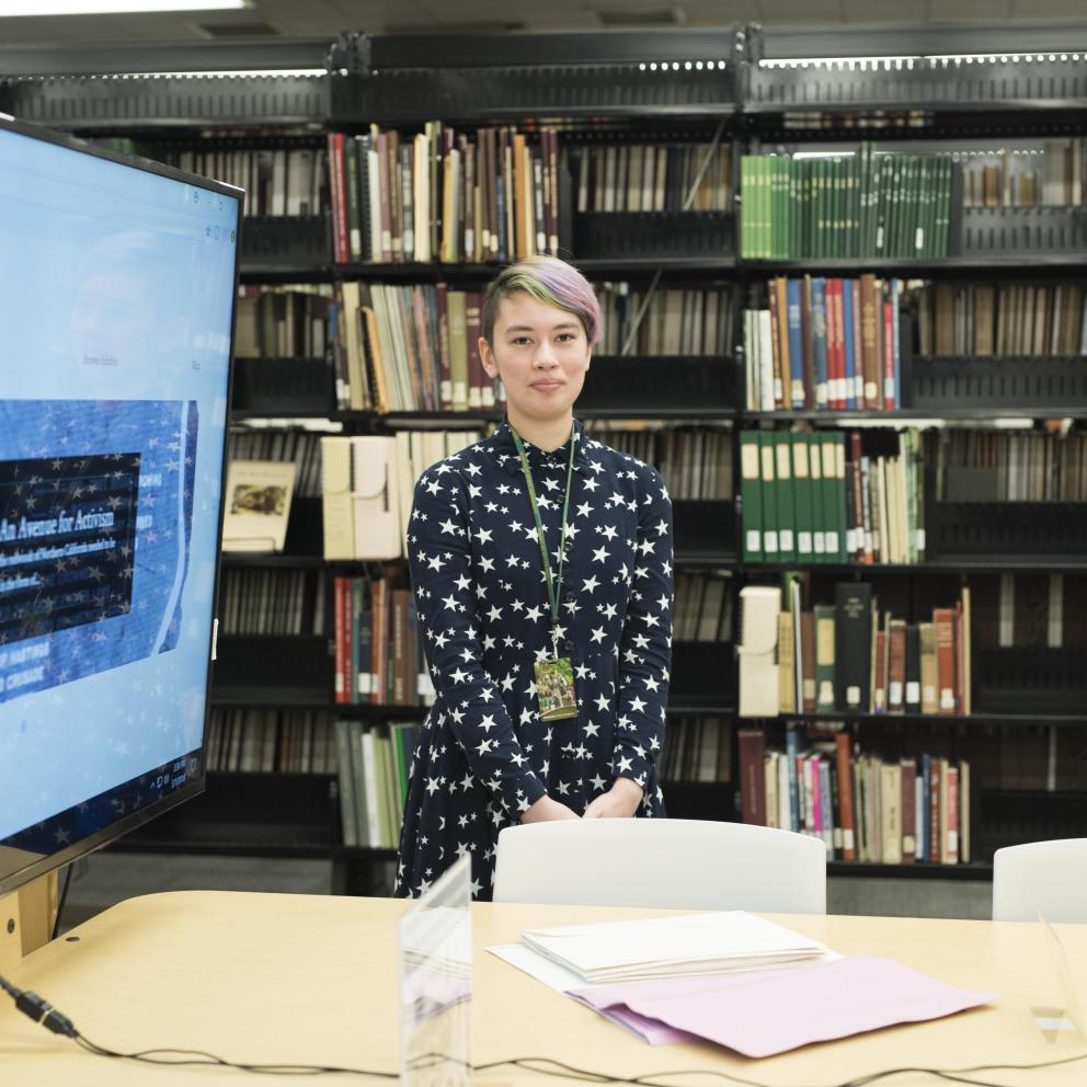 Student standig in front of a library book case with a large computer screen to the left