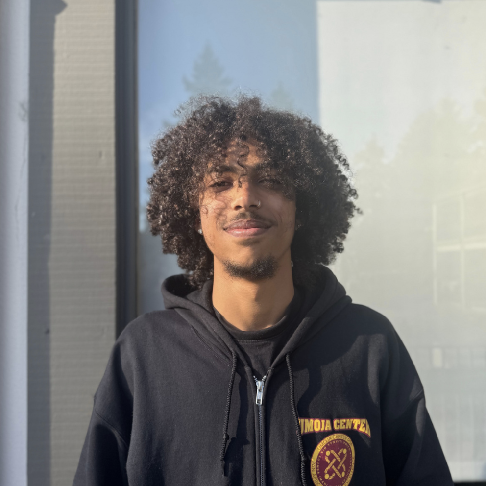 Kai smiles in an outdoor setting in his Umoja Staff hoodie.