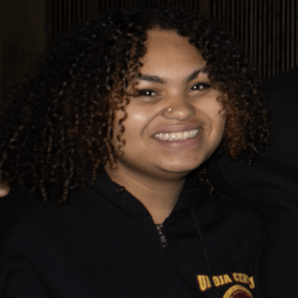 Jei smiles for a photo wearing their Umoja center staff hoodie.