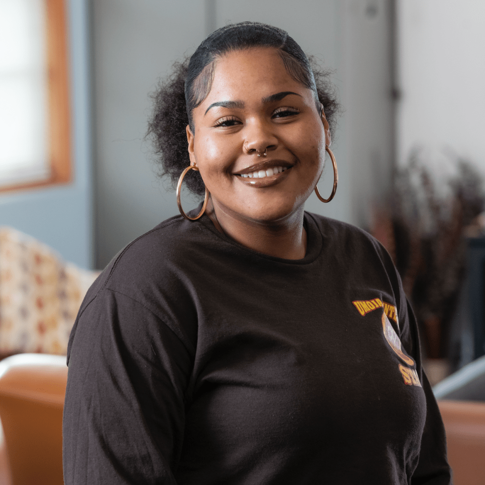 Delaena smiles in her staff shirt with large gold hoops.