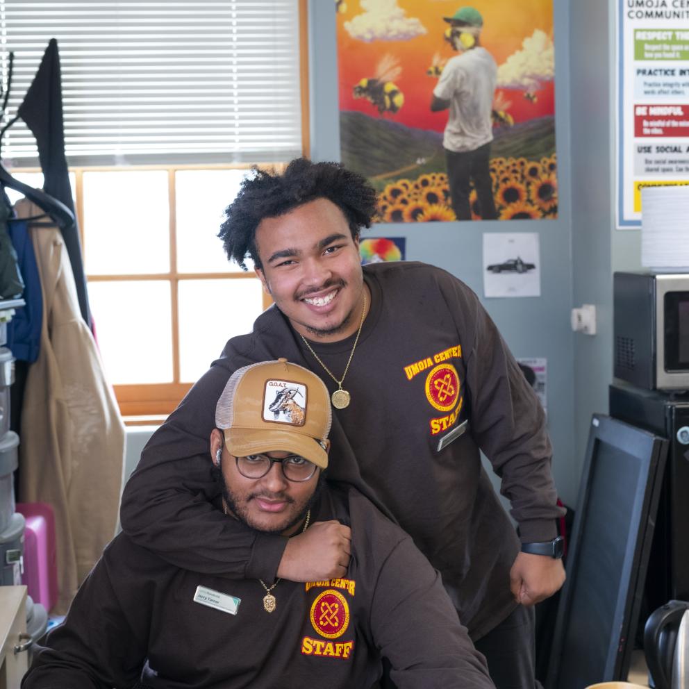 Two student staff embrace and smile for a photo at the Umoja Center Front Desk