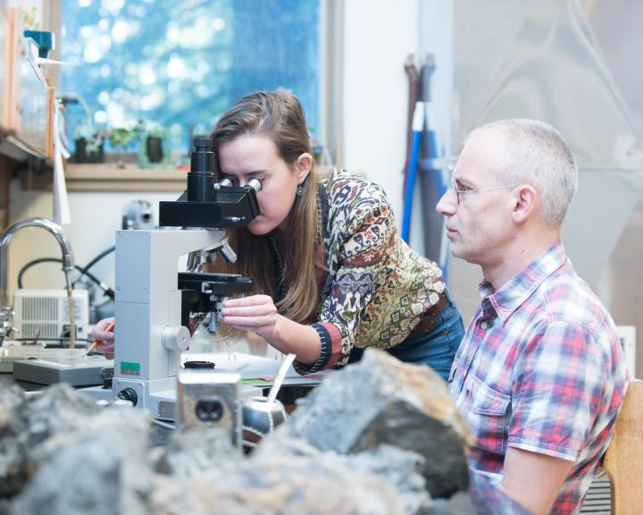 student looking into a microscope with a teacher sitting next to them