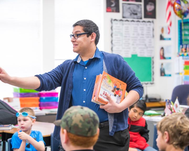 teacher holding books talking to kids with his finger pointing at something