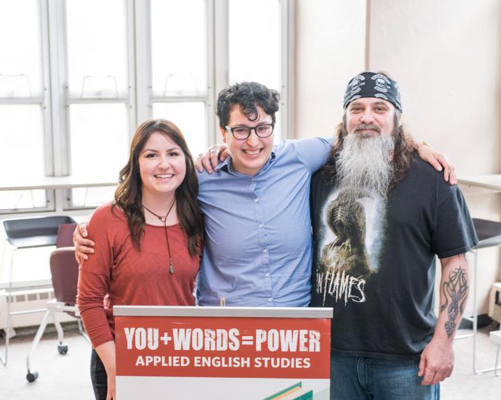 three people standing shoulder to shoulder holding a sign that says YOU + WORDS = POWER