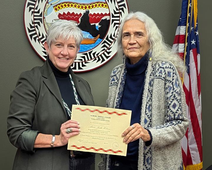 A woman with short grey hair receiving a bar exam certification from a woman with long grey hair