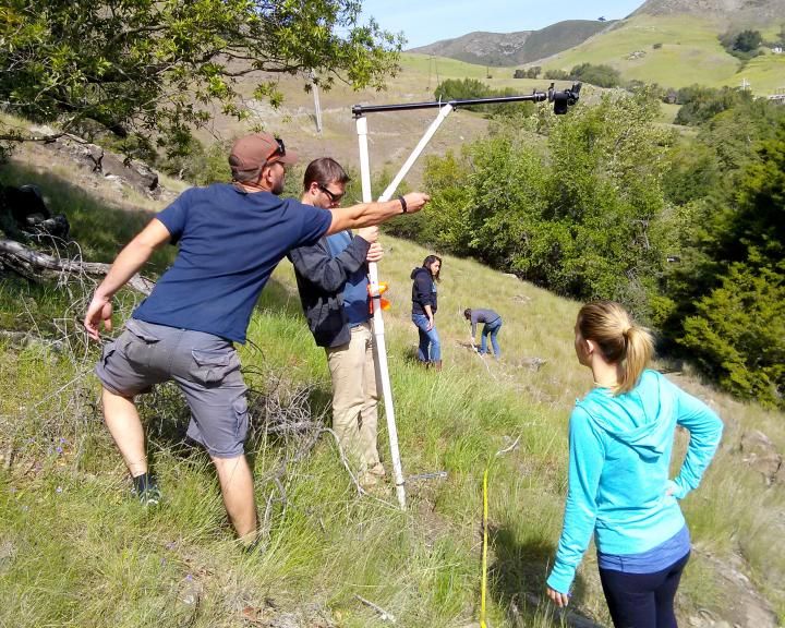 Students with equipment, working on a grassy hillside