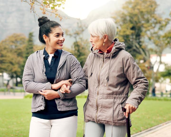 Young eldercare staff member walking with older woman