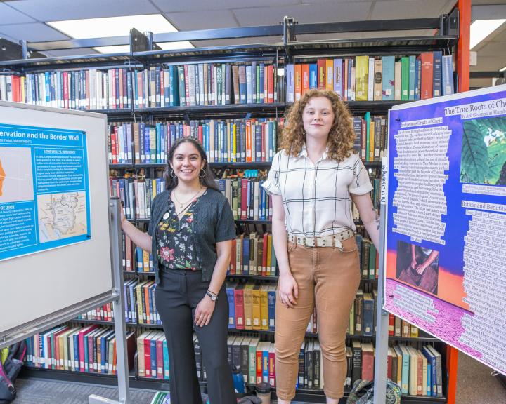 Two students standing in front of the book stacks presenting posters