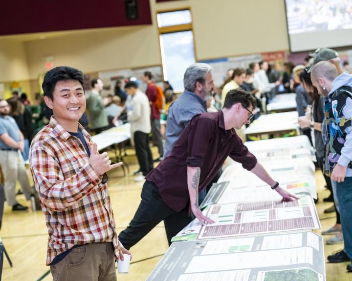 Student presenter looking at the camera standing near his research poster