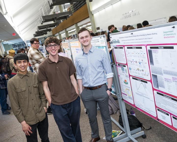 3 male students standing next to their research poster