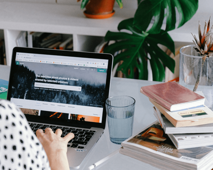 Someone typing on a laptop on desk in home office with stack of books next to them